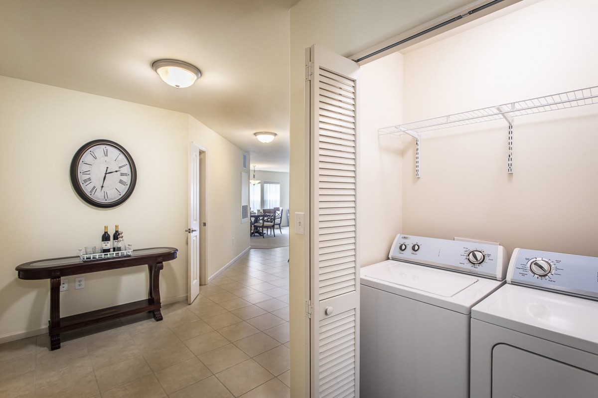 A well-lit hallway with a compact laundry area featuring a washer and dryer behind folding doors.