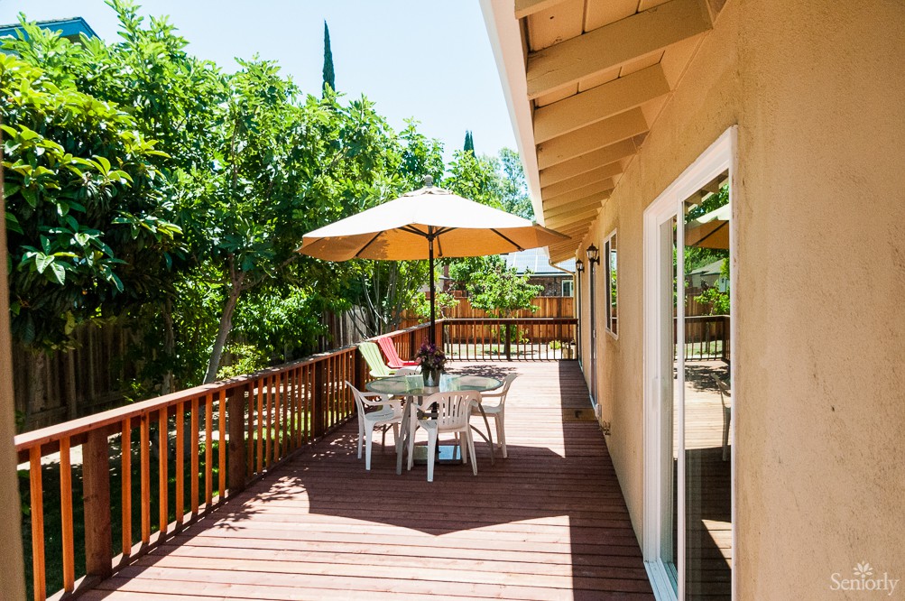 A sunny outdoor patio with a table, chairs, and an umbrella surrounded by lush greenery.