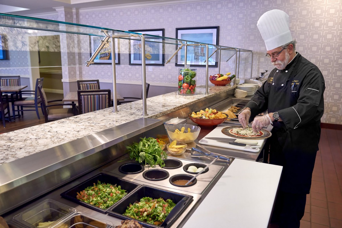 A chef preparing a dish at a buffet counter with various ingredients on display.