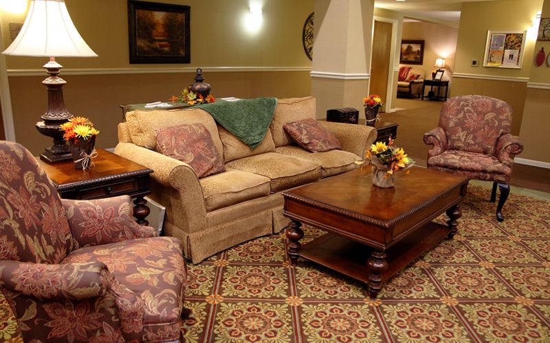 A cozy living room with a sofa, armchair, and wooden coffee table arranged on a patterned carpet.
