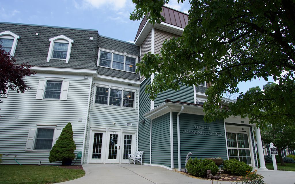 A residential building with a light blue exterior and multiple windows, surrounded by trees.