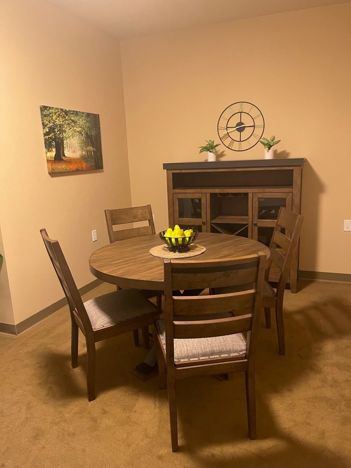 Cozy dining area with a round table and wooden chairs, complemented by a cabinet and wall decor.