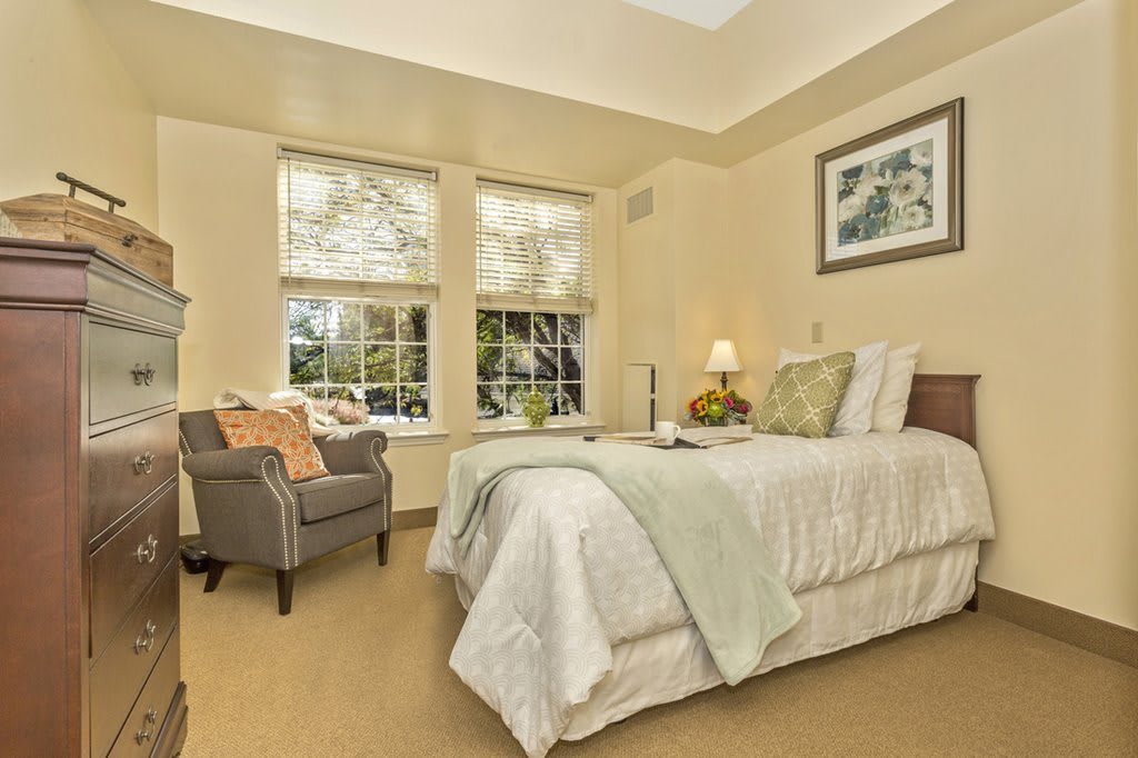A cozy and elegantly designed bedroom with a comfortable bed, an armchair by the window, and tasteful decor.