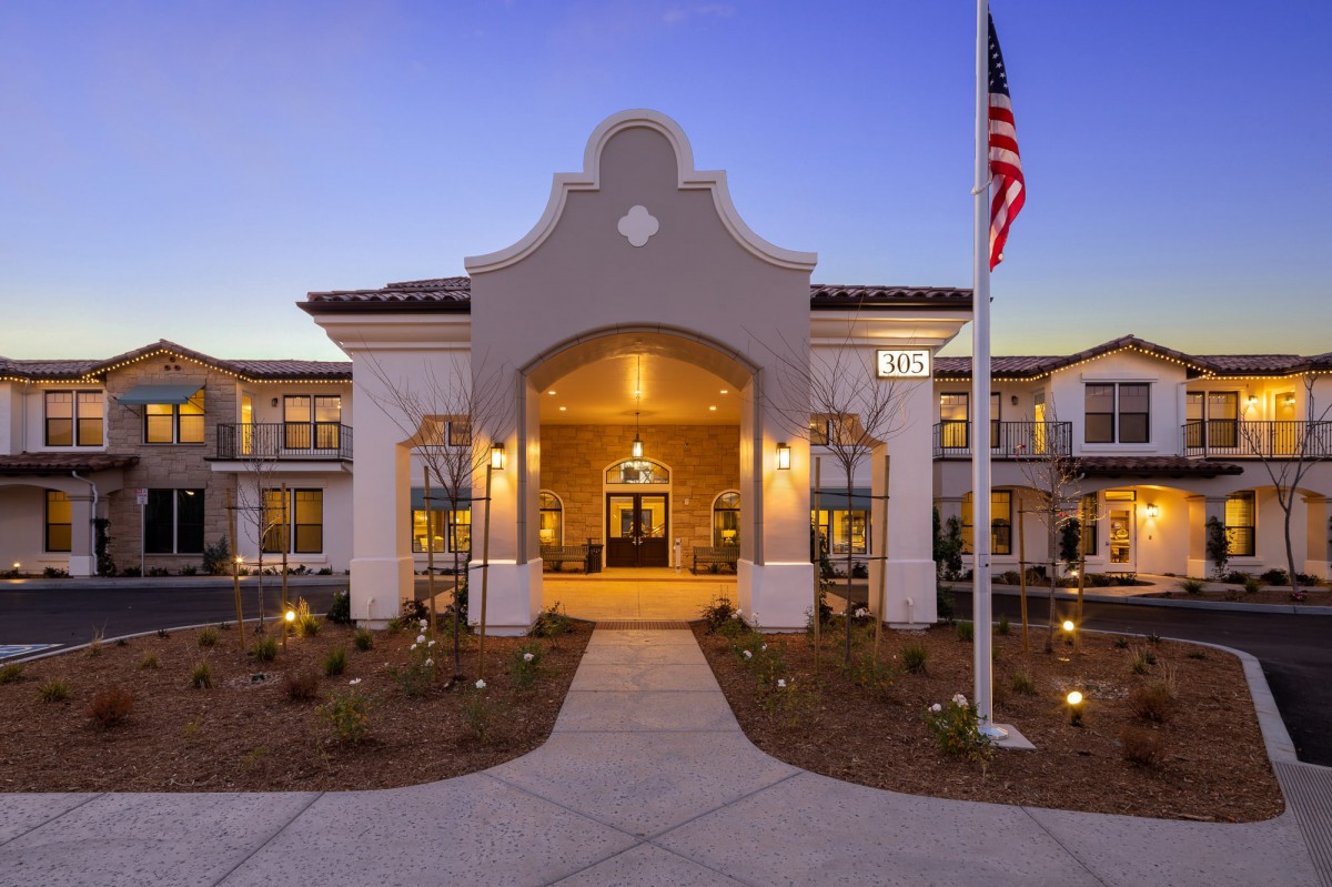 An illuminated building entrance with a flagpole at dusk.