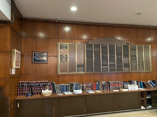 A polished wooden wall featuring a collection of books and name plaques, illuminated by soft lighting.