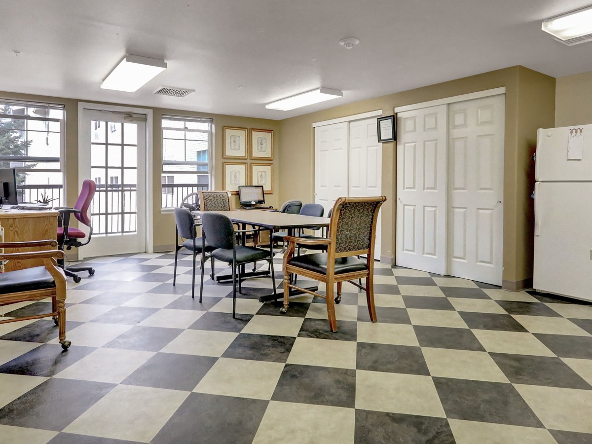 A meeting room with a checkered floor, featuring a table surrounded by chairs and natural light from the windows.