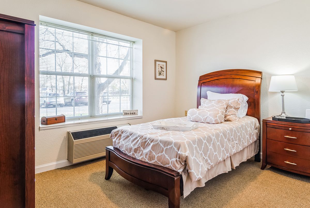 A cozy bedroom featuring a single bed with decorative pillows and a large window.