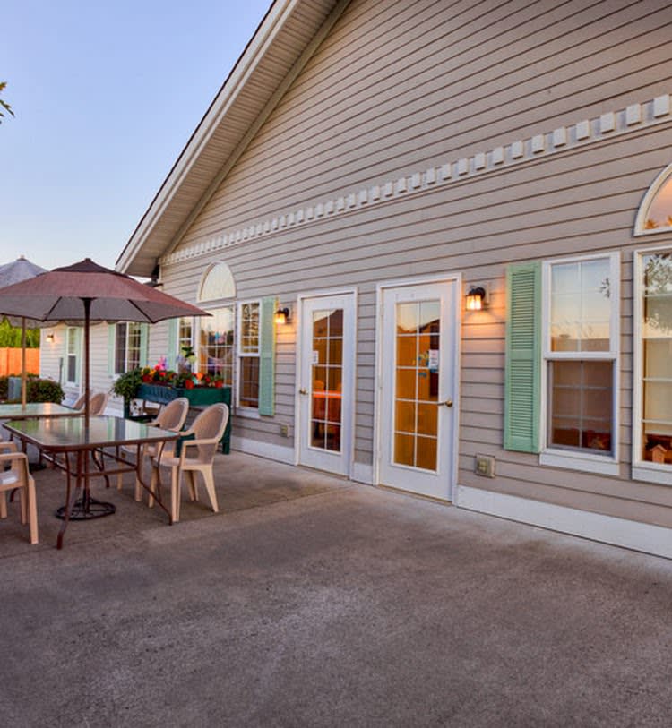 A cozy patio area with outdoor furniture and an umbrella on a concrete surface, adjacent to a house with multiple windows.