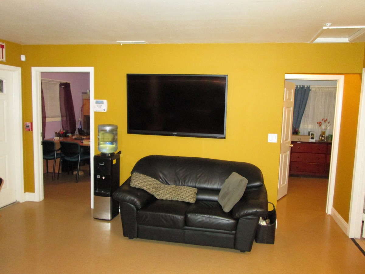 A cozy living room with a black sofa and a large television mounted on a yellow wall.