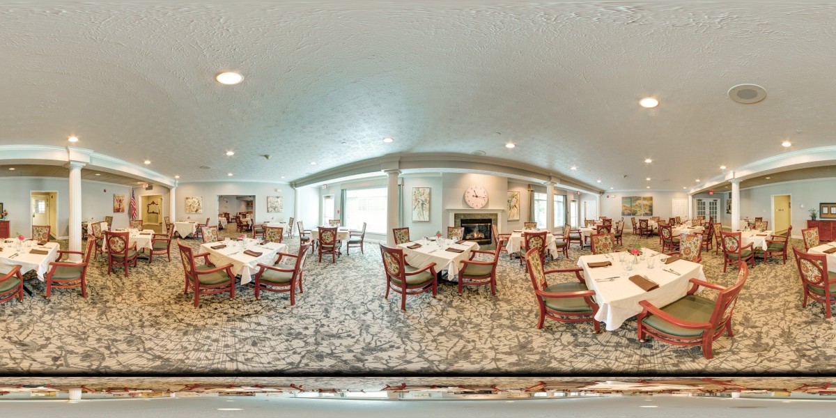 A spacious dining room with elegantly set tables and chairs, featuring a fireplace and carpeted floors.