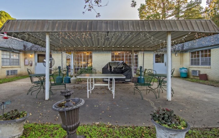 A backyard patio featuring a covered area with a table, chairs, and a grill.