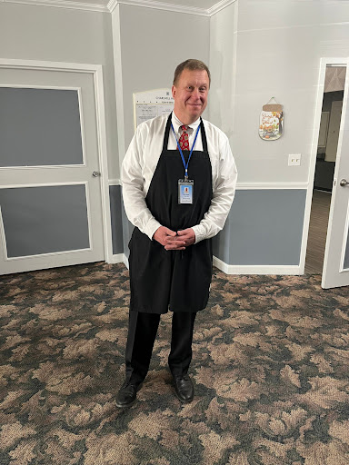 A man in formal attire wearing an apron, ready to assist at an event.