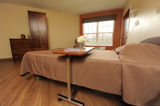 A cozy and well-lit bedroom featuring a neatly made bed, a small table, and decorative flowers.