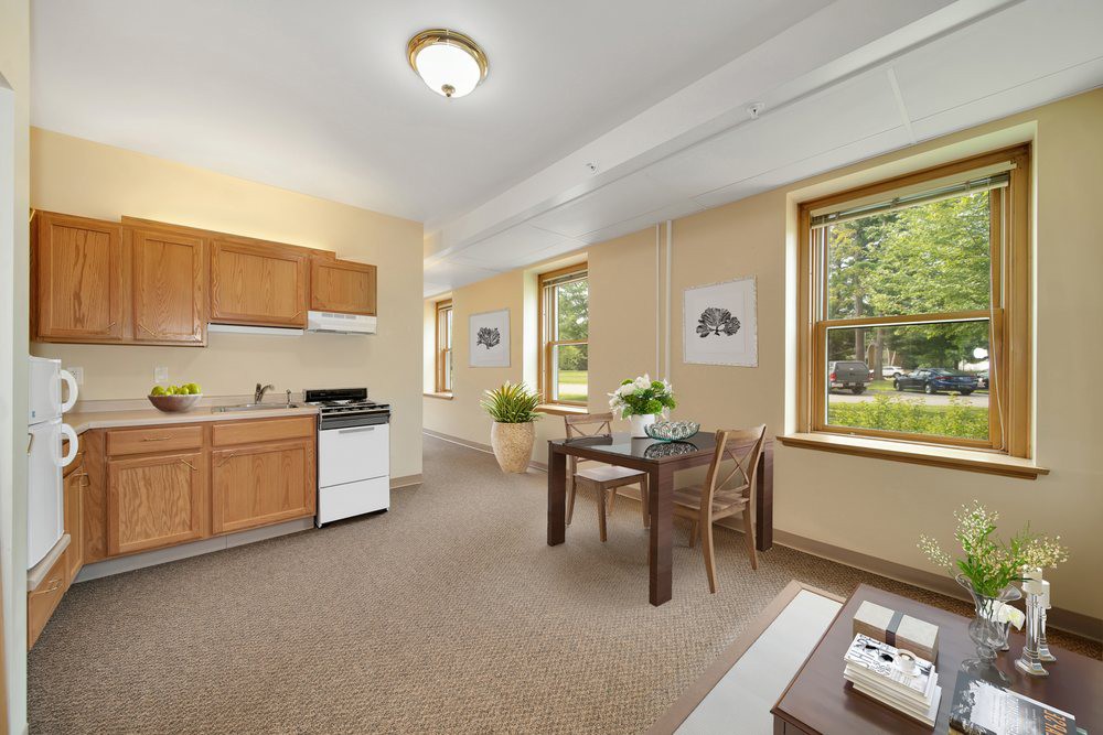 A cozy apartment interior featuring a small kitchen and dining area, with ample natural light from large windows.