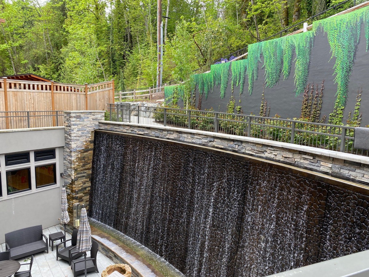 A serene outdoor patio featuring a cascading waterfall with lush greenery and a painted mural wall.