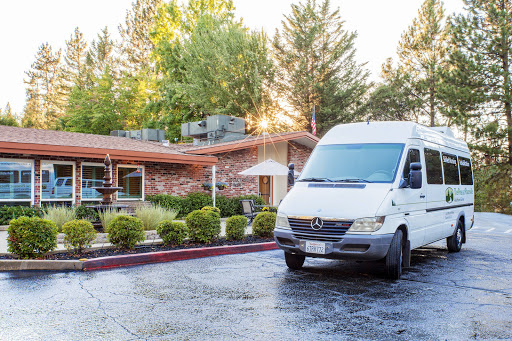 A white van parked in front of a modern building surrounded by trees and greenery, illuminated by the morning sun.