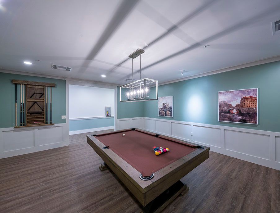 A modern billiards room with a pool table, stylish lighting, and artwork.