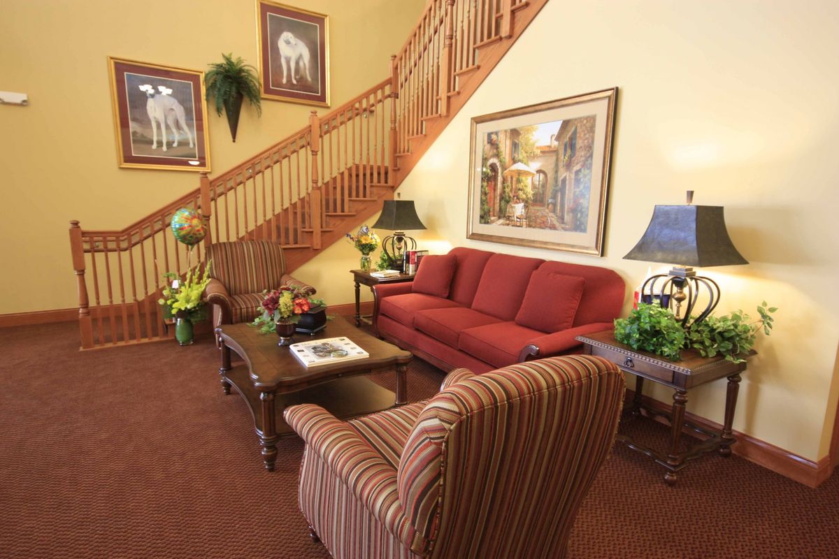 A cozy living room featuring a red sofa, striped armchair, and decorative paintings near a wooden staircase.
