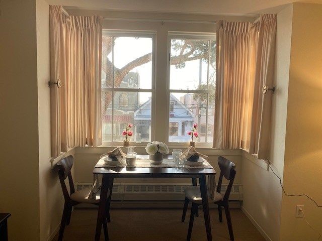 A cozy dining nook with a table set by a window, adorned with vases of flowers and surrounded by flowing curtains.