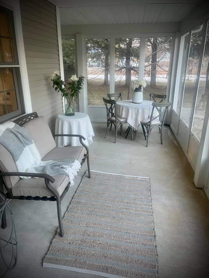 A cozy porch featuring a bench, a table with chairs, and a vase with flowers.