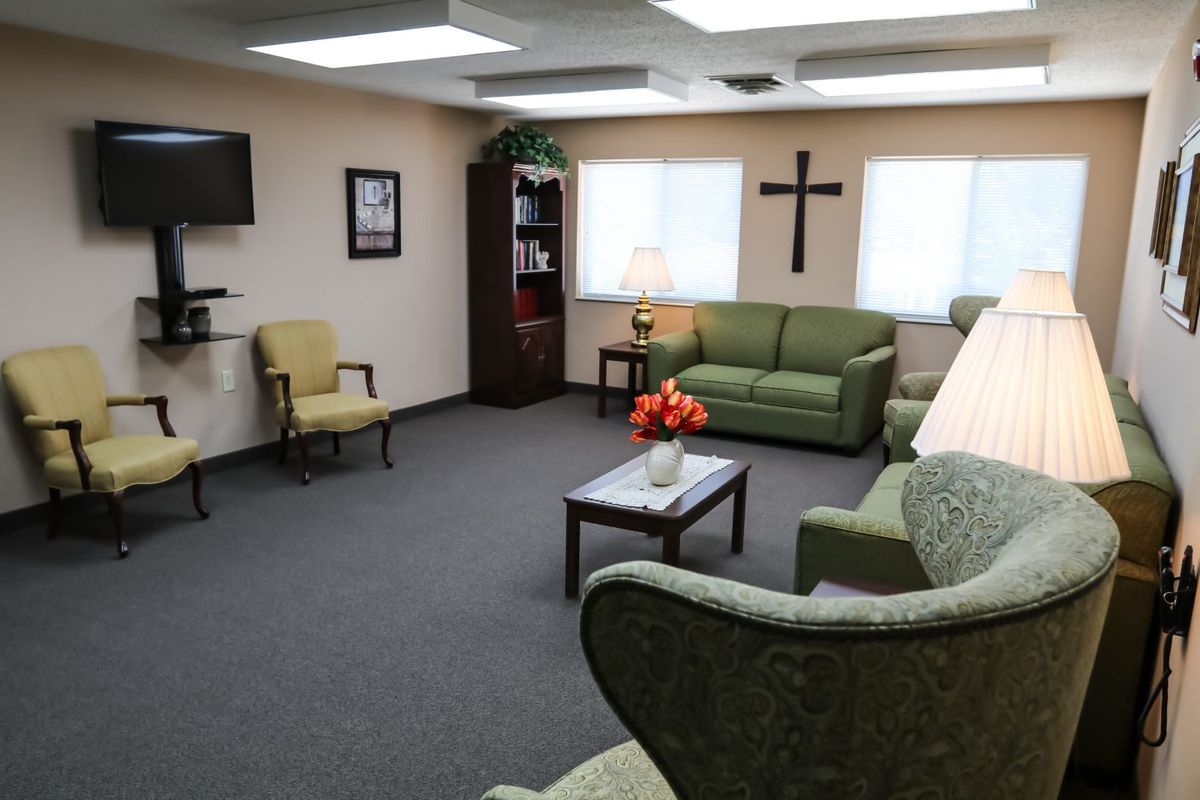 A comfortable and cozy waiting room with sofas, chairs, a lamp, and a cross on the wall.