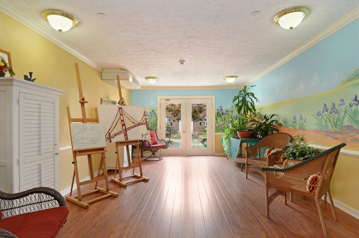 A bright and inviting art studio with easels, plants, and a wooden floor.