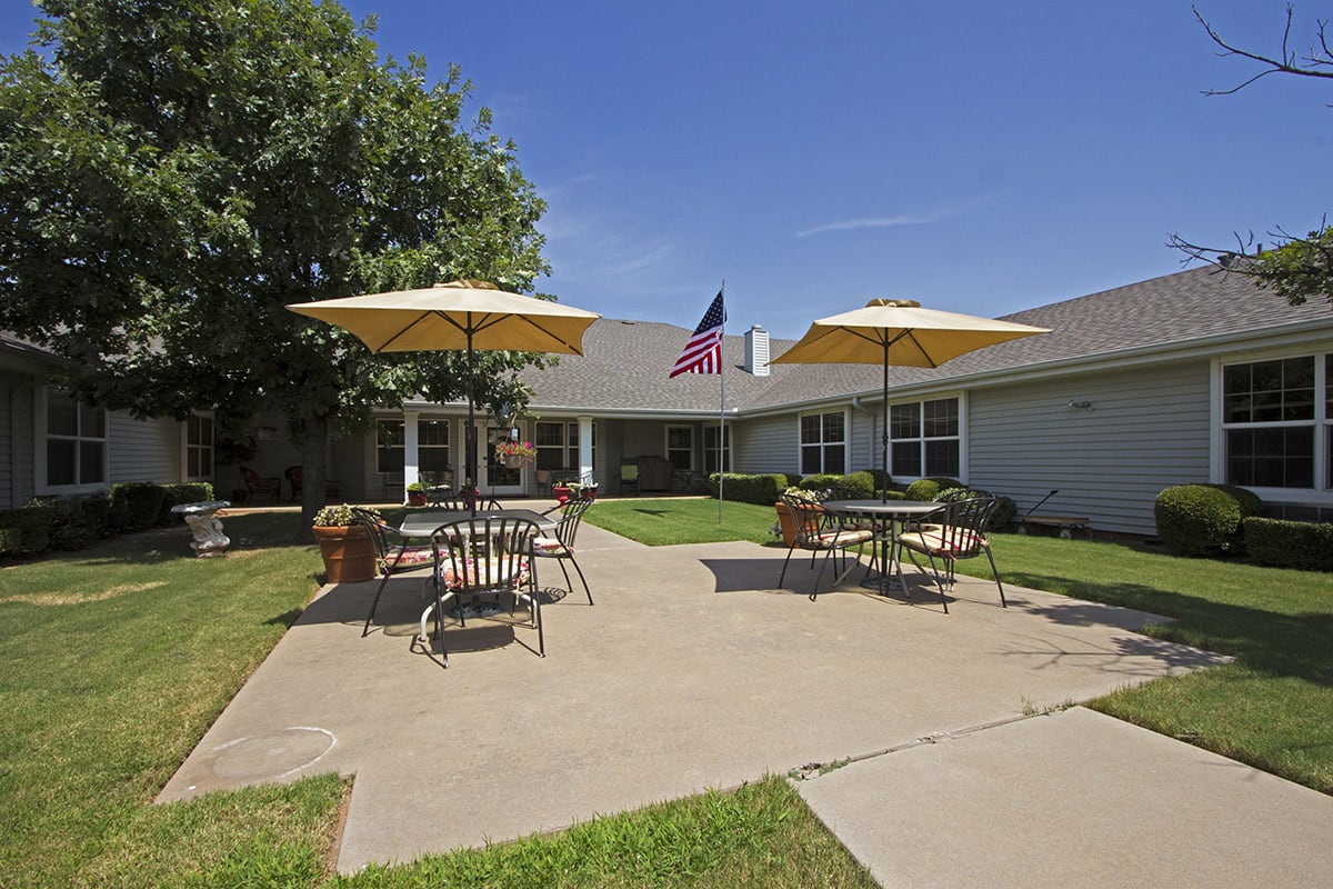 A sunny patio with tables, chairs, and umbrellas in front of a building adorned with flags.