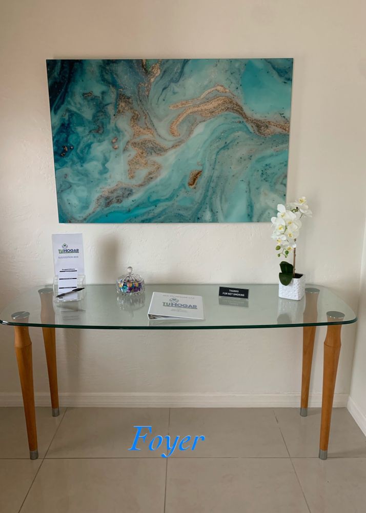 A glass table in an interior setting with a decorative orchid plant and abstract artwork on the wall.