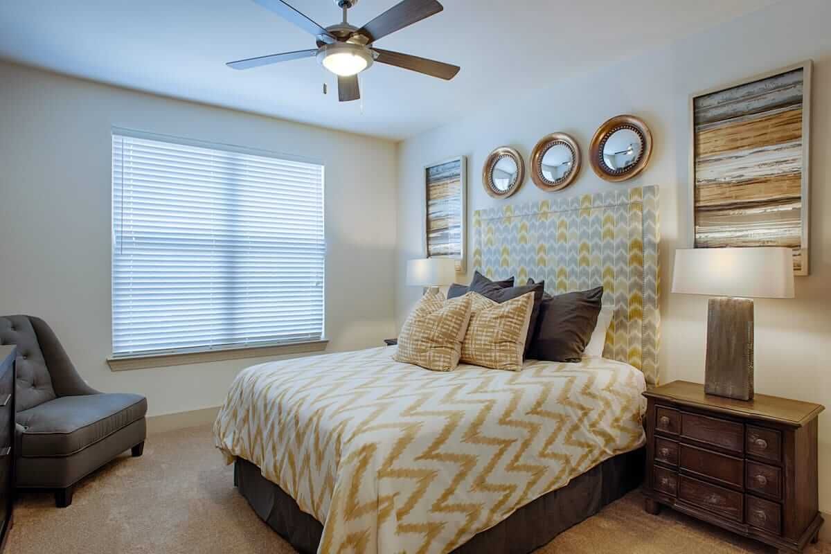 A modern bedroom with stylish decor, featuring a comfortable bed, decorative pillows, wall art, and a ceiling fan.