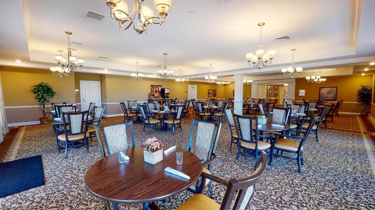 A spacious and elegantly decorated dining room with multiple tables and chairs, illuminated by chandeliers.