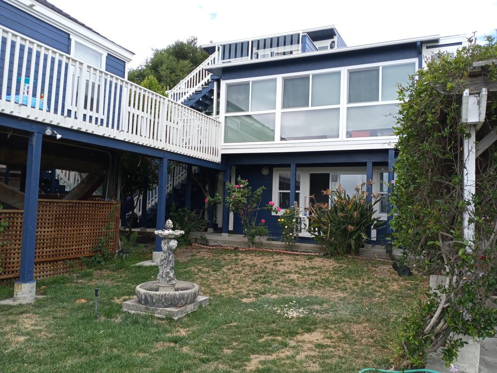 A two-story house with a balcony, featuring a small garden and fountain in the yard.
