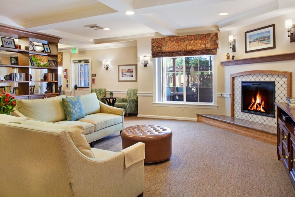 A cozy living room featuring a sofa, armchair, fireplace, and large window with decorative elements.