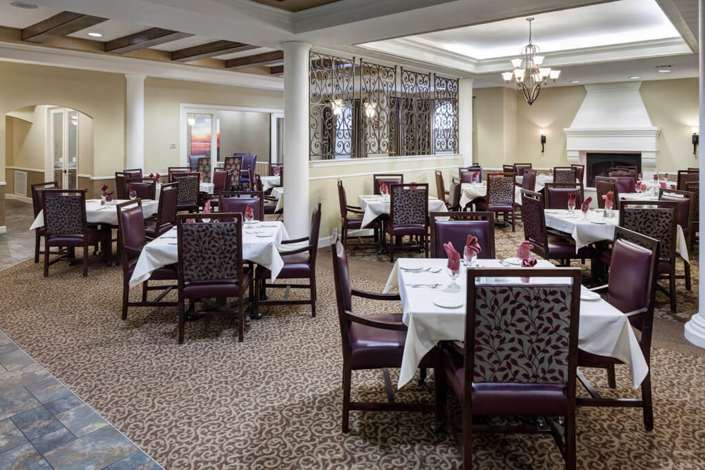 An elegant restaurant dining room with neatly arranged tables and chairs, featuring chandeliers and a patterned carpet.