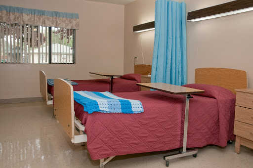 A clean and organized patient room in a healthcare facility, featuring two beds and decorative curtains.