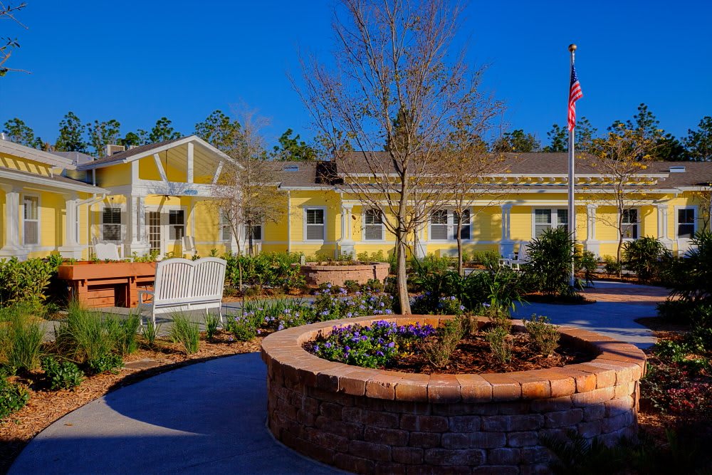 A bright yellow building with a landscaped garden and flag under a clear blue sky.
