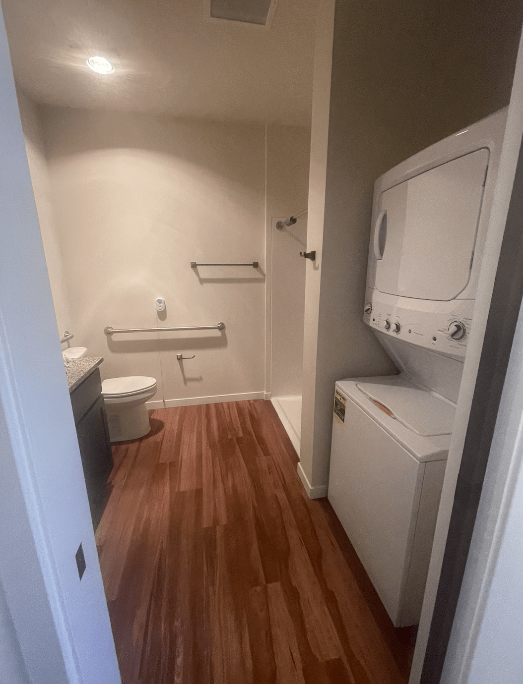 A bathroom equipped with a stackable washer and dryer, featuring wood flooring.