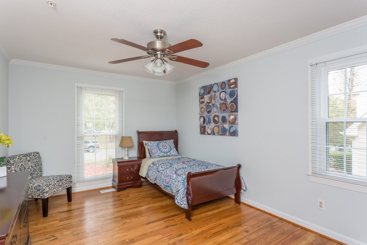 A simple bedroom with a single bed, wooden flooring, and a ceiling fan.