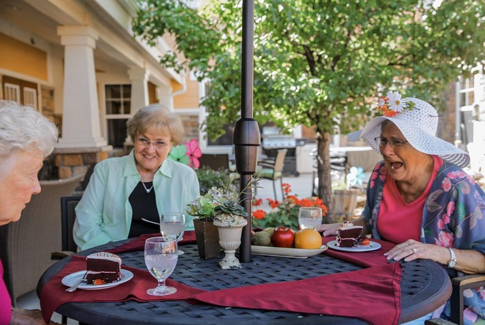 Two elderly women enjoying a meal together on a sunlit patio.