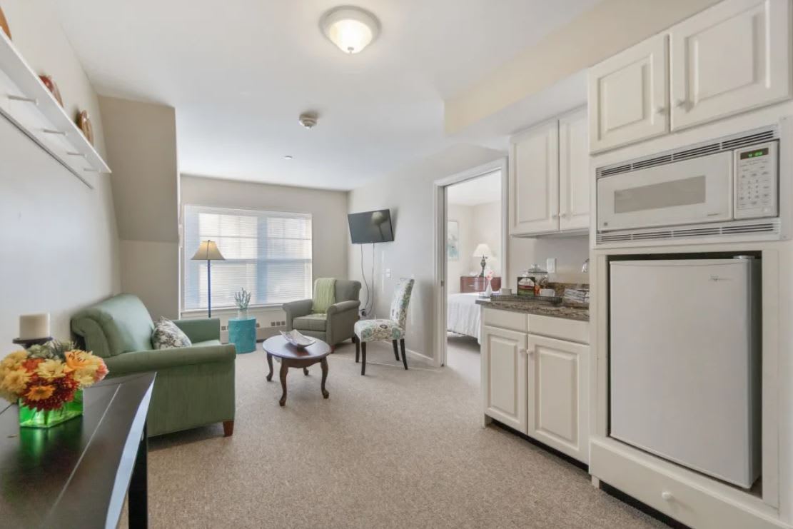A modern apartment living room with a kitchen area, featuring cozy furniture and bright lighting.
