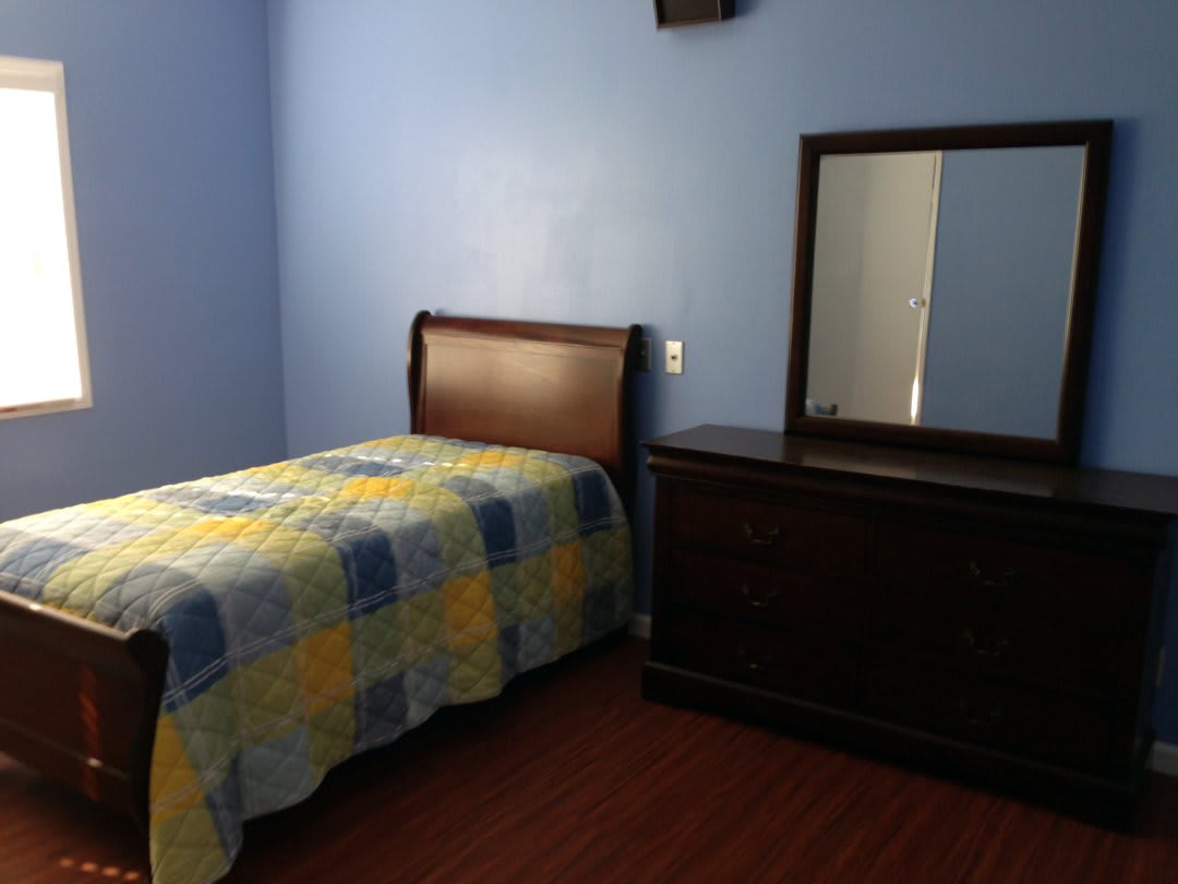 A simple bedroom with a single bed and wooden furniture against blue walls.