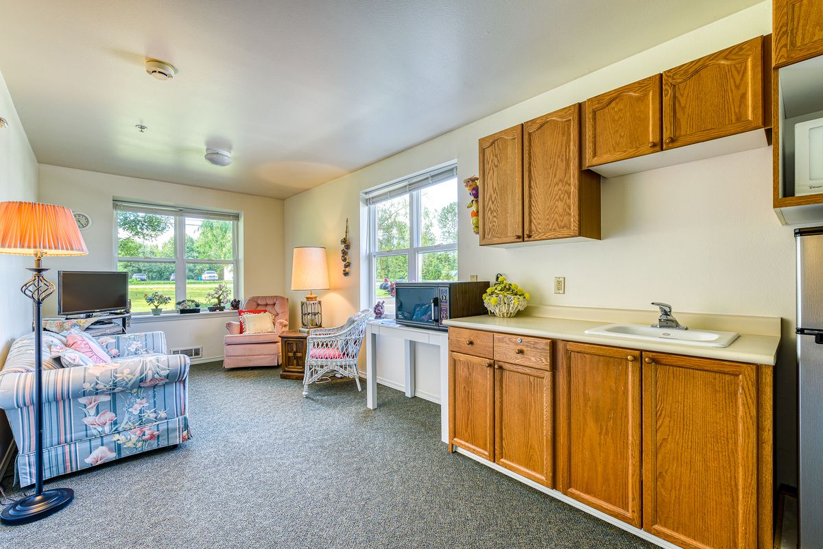 A cozy living area with a kitchenette, featuring comfortable seating and large windows.