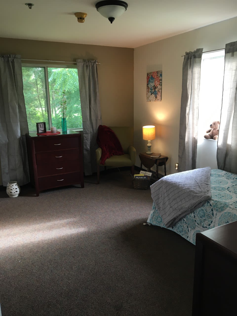 A cozy bedroom with a bed, dresser, and chair near the window.