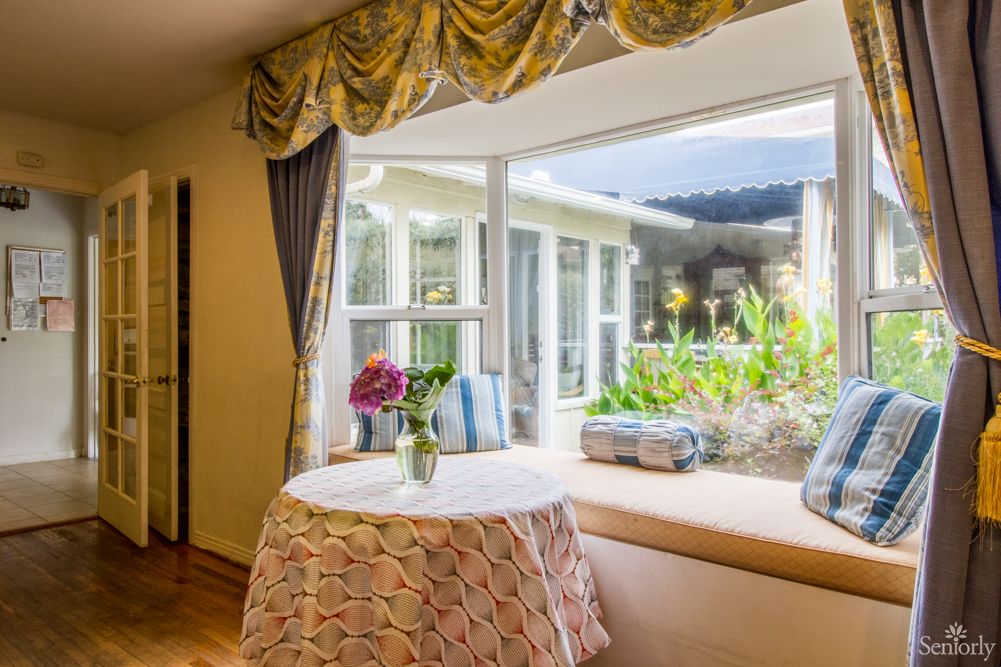A cozy living room with a large window, floral arrangements on the table, and elegant curtains.