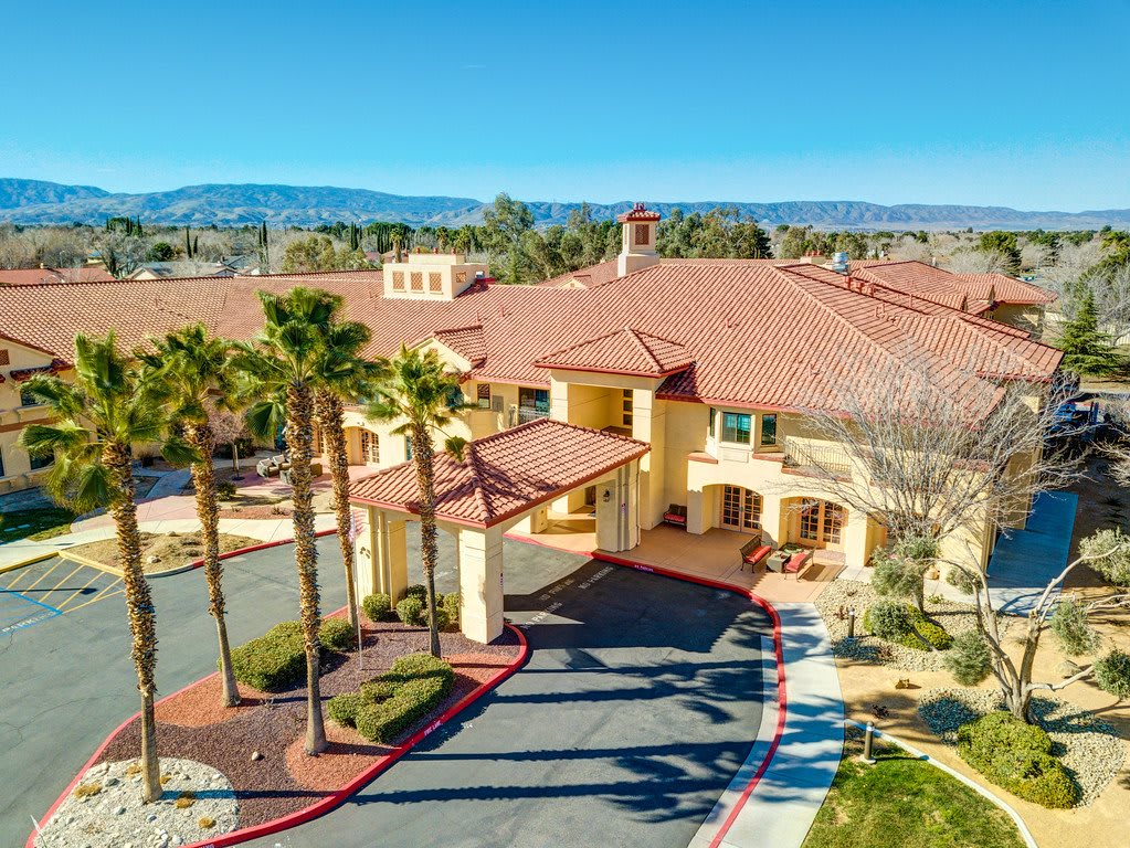 Aerial view of a large building surrounded by palm trees with mountains in the background.