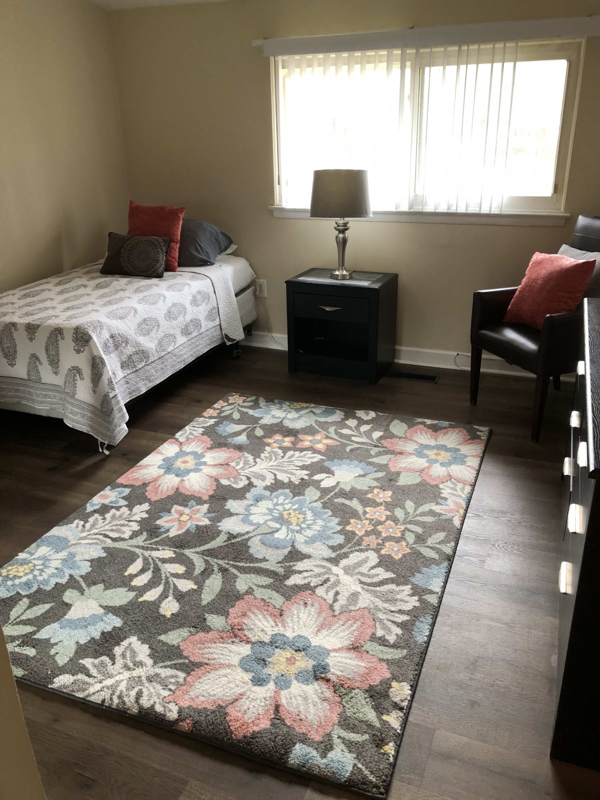 A cozy bedroom with a single bed, floral rug, and natural lighting.
