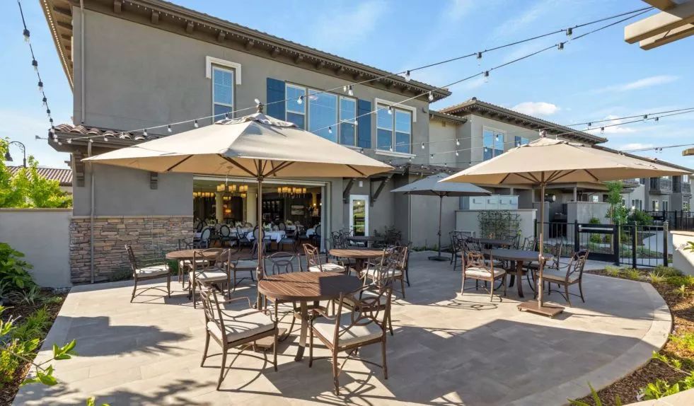 A sunny outdoor patio area with tables, chairs, and large umbrellas at a restaurant.