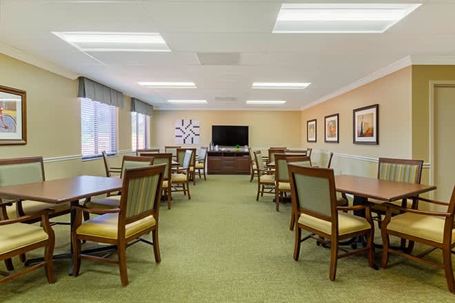 A spacious conference room with multiple tables and chairs, featuring a television and wall decorations.