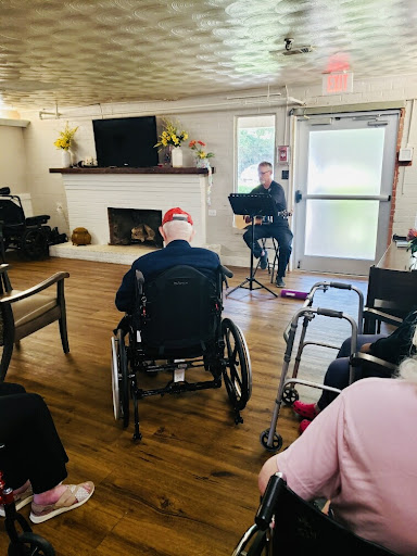 A performer entertains a group of elderly residents in a community room, creating a warm and lively atmosphere.