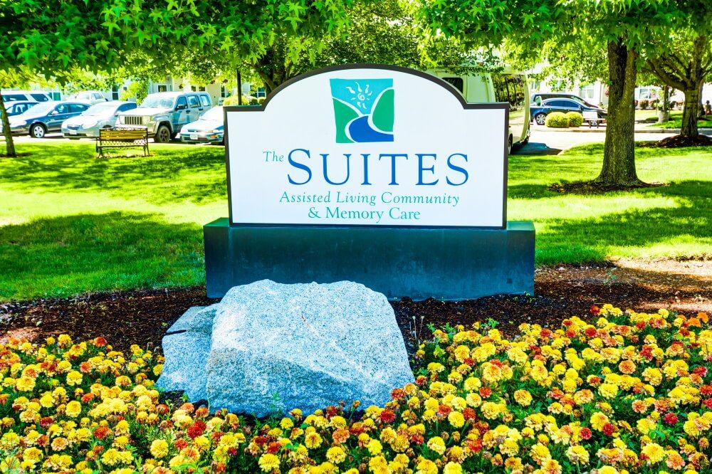 A landscaped sign for 'The Suites' healthcare center surrounded by flowers.