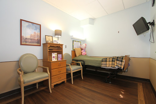A cozy hospital room featuring a bed, two chairs, and personal touches.